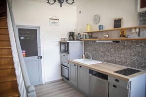 A compact kitchen with a microwave, oven, and dishwasher. There is a chalkboard with a message, a clock, and a shelf with decorative items.