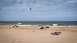 En strand med suserende drager, få mennesker og et roligt hav.