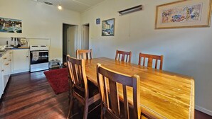 A dining area with a wooden table and chairs, a kitchen with a stove and oven, and a hallway leading to another room. - Bethanga - Short walk to the heart of Robe -Pets Welcome - Outside Only (Robe)