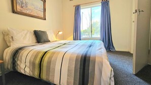 A hotel room with a bed, a nightstand, a lamp, a window with curtains, and a painting on the wall. - Bethanga - Short walk to the heart of Robe -Pets Welcome - Outside Only (Robe)
