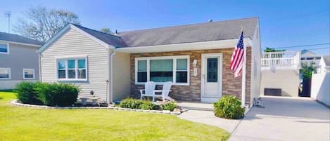 A single-story house with a front porch, a small lawn, and an American flag.