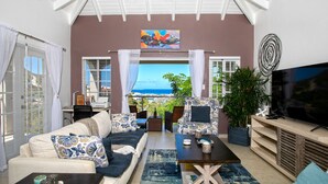A living room with a sofa, coffee table, TV, and a view of the ocean. - Centrally located minutes away from great beaches, town center and French side. (Philipsburg)