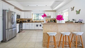 A modern kitchen with white cabinets, stainless steel appliances, a large island with bar stools, and decorative butterflies on the wall. - Centrally located minutes away from great beaches, town center and French side. (Philipsburg)