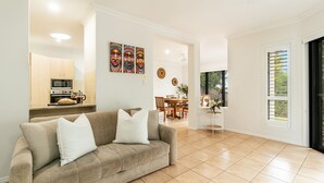 Een moderne woonkamer met een beige bank, een eetgedeelte met houten meubels, en een keuken met een magnetron en oven.