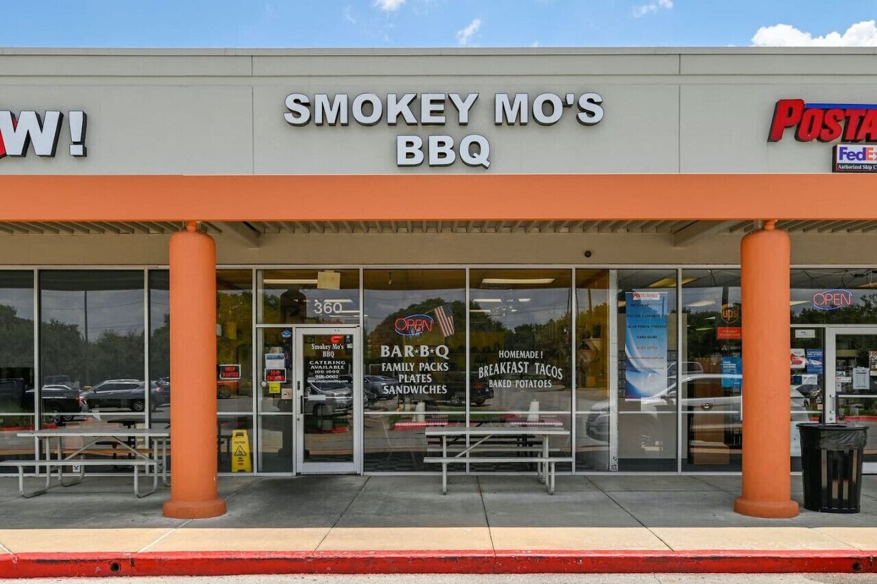 A Smokey Mo's BBQ storefront with a FedEx Express sign, outdoor seating, and a clear view of the entrance.