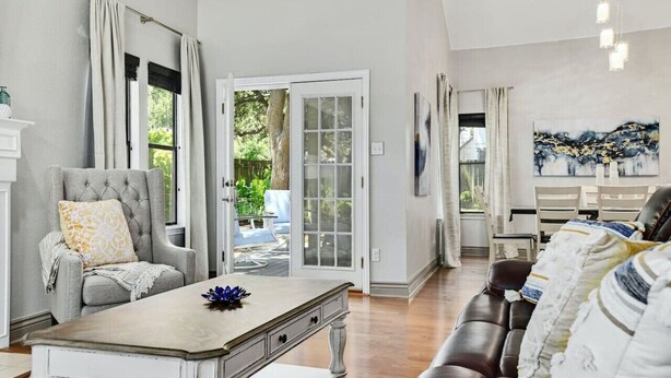 Una sala de estar con un sillón gris, una mesa de centro y un sofá. Hay una puerta que da a un balcón.