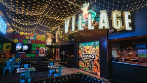 Un cine con un letrero de neón que dice "VILLAGE" y "ALAMO DRAFTHOUSE CINEMA" en la pared.
