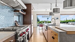 A modern kitchen with a large island, stainless steel appliances, and a view to the outdoors.