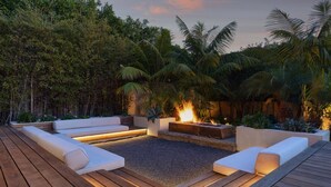 A deck with a fire pit, seating, and a garden with trees and plants.