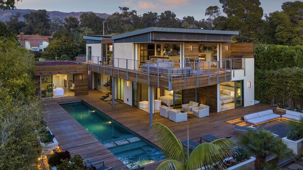 A modern two-story house with a rooftop deck, a swimming pool, and lush landscaping.