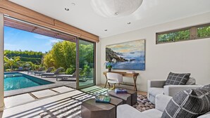 A modern living room with a pool, a large window with a view of greenery, and a painting on the wall.