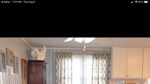 A dining area with a wooden table and chairs, a decorative ceiling fan, and a kitchen area with white cabinets and a red appliance. - Fin's Fish Camp at Harker's Island (Harkers Island)