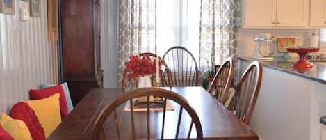 A dining area with a wooden table and chairs, a vase with flowers, and a kitchen area with cabinets and appliances.