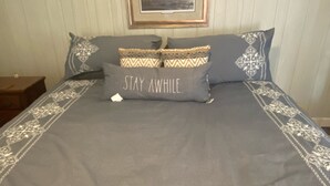 A neatly made bed with a grey bedspread and decorative pillows, including one with the text "STAY AWAY". - Fin's Fish Camp at Harker's Island (Harkers Island)