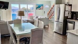 A spacious kitchen with a dining area, featuring a glass-top table, wicker chairs, and modern appliances. - Ocean View House, Steps to Beach, Pet Friendly, Linens & Beach Gear Provided (Surf City)