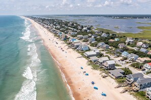 Une vue aérienne d’une ville côtière avec une longue plage de sable, des maisons et une vue dégagée sur l’océan.