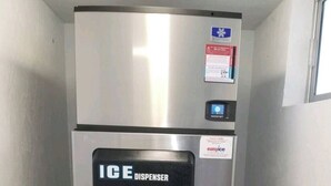 A stainless steel ice dispenser refrigerator with a water dispenser, located in a narrow hallway with tiled flooring. - Brand New Pool on Daytona Beach!! (Daytona Beach)