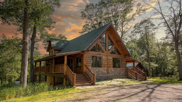 A log cabin with a wooden deck, a staircase, and a stone foundation. - Northwoods Log Cabin (Danbury)