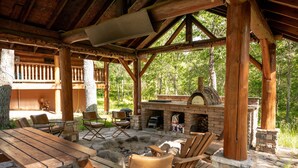 An outdoor patio with a stone fireplace, wooden chairs, and a large table. - Northwoods Log Cabin (Danbury)