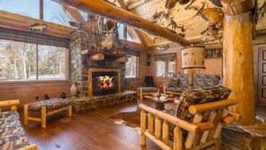 A rustic lodge interior with a stone fireplace, wooden furniture, and taxidermy mounted on the ceiling. - Northwoods Log Cabin (Danbury)