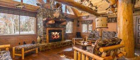 A rustic lodge interior with a stone fireplace, wooden furniture, and taxidermy mounted on the ceiling.
