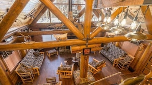 A rustic wooden interior with a high ceiling, wooden beams, and a variety of seating arrangements including sofas and chairs. - Northwoods Log Cabin (Danbury)