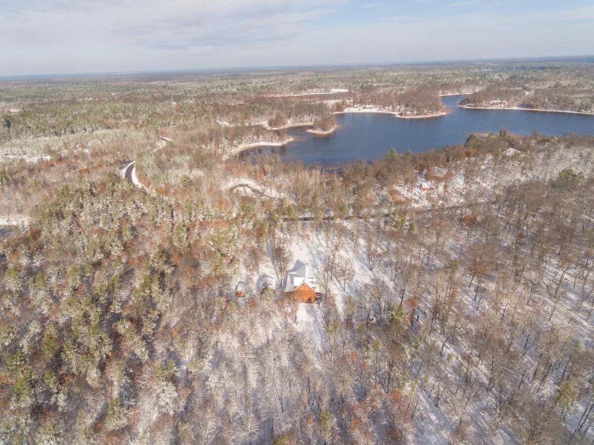 Una cabaña aislada rodeada de un bosque con un lago y un camino sinuoso.