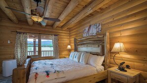 Un dormitorio de cabaña de madera con una cama, dos lámparas de noche, un ventilador de techo y una ventana con cortinas.