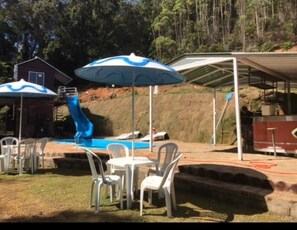 Relax by the pool with a slide and outdoor seating, shaded by two umbrellas.