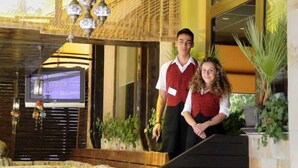 Un hombre y una mujer de pie en un vestíbulo con un televisor, plantas y una estructura de madera.