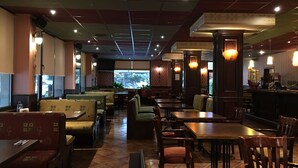 Un restaurante con cabinas y mesas, una zona de bar y un ventanal con vistas a árboles.