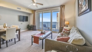 Una sala de estar con comedor, un ventilador de techo, un televisor y un balcón con vista al mar.