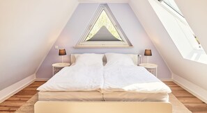 A bedroom with a sloped ceiling, a skylight, and a bed with white bedding.
