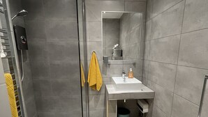 Een moderne badkamer met een douchecabine van glas, een witte wastafel en een gele handdoek.