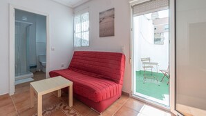 Ein rotes Sofa, ein kleiner Tisch und eine Glastür zum Balkon mit Gartenmöbeln.