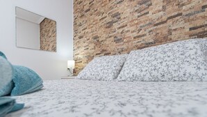 Ein Schlafzimmer mit einem Ziegelmuster-Kopfteil, einem Bett mit floralem Bettbezug, einer Nachttischlampe und einem Spiegel an der Wand.