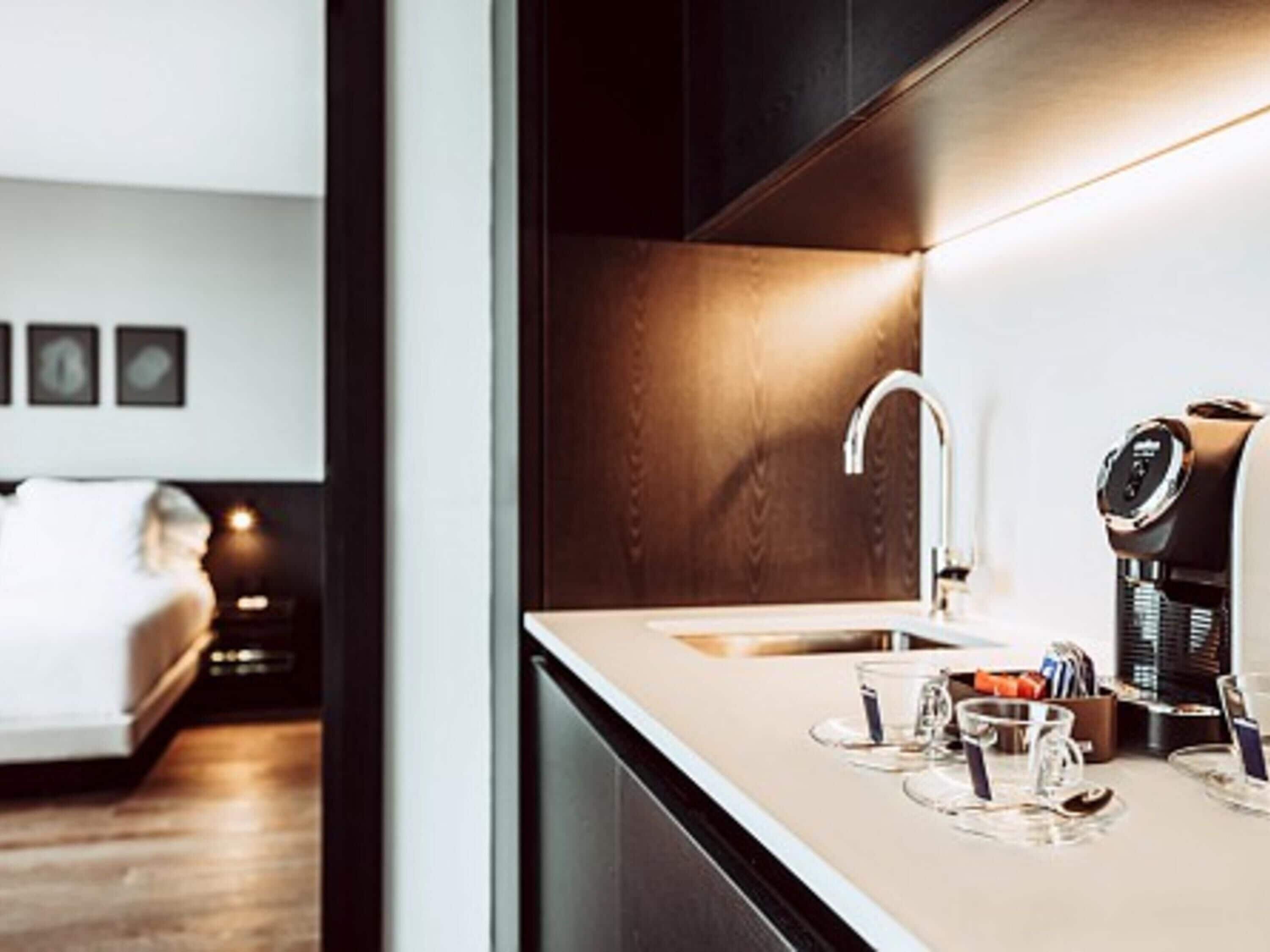 A modern kitchen with a built-in coffee machine, a sink, and a countertop with glasses and a coffee pot.