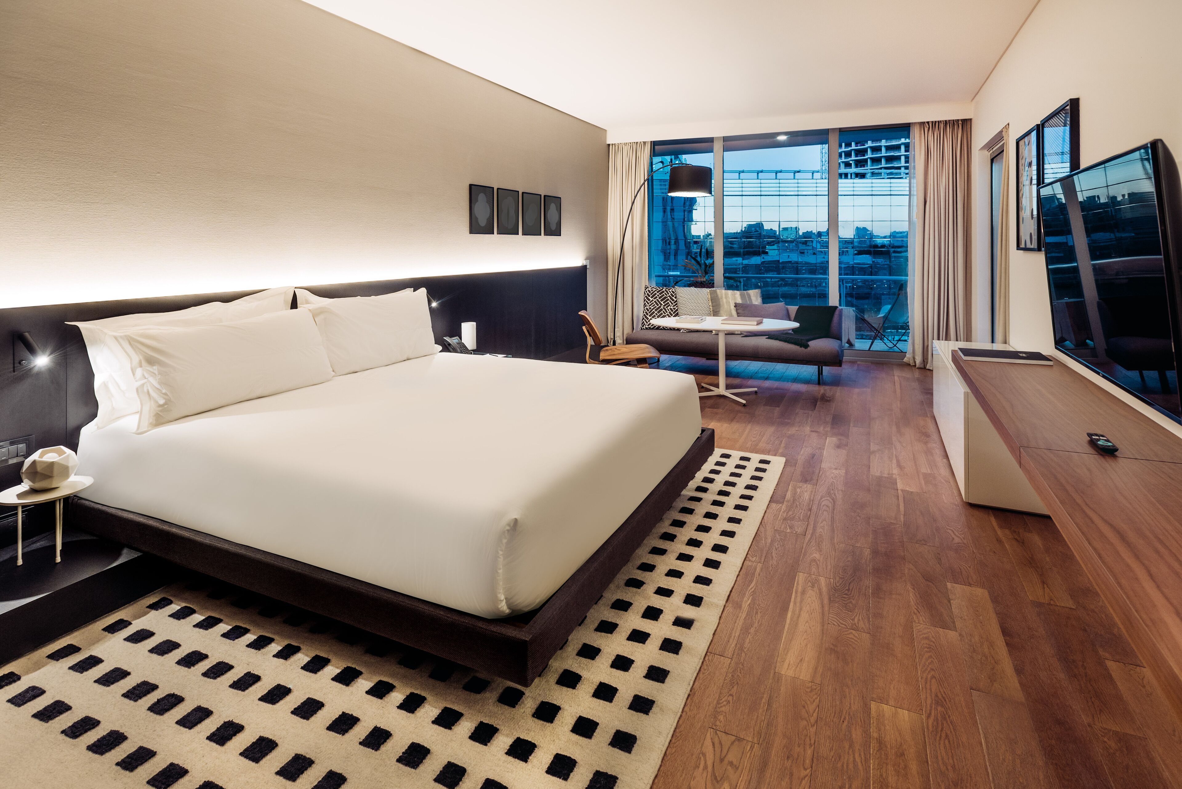 Een moderne hotelkamer met een groot bed, een bank, een televisie en uitzicht op de stad.