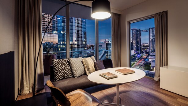 A modern living room with a sofa, a round table, and a view of a cityscape through large windows. - SLS Buenos Aires Puerto Madero (Buenos Aires)