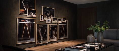 Un salon moderne avec un mur de couleur sombre, des photographies encadrées, une table basse avec des livres et un canapé gris.
