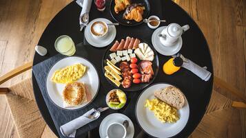 Una mesa redonda con alimentos para el desayuno, como huevos, tostadas, salchichas, queso y croissants.