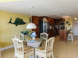 A dining area with a glass table and wicker chairs, a kitchen with wooden cabinets and stainless steel appliances, and a decorative fish on the wall. - Ocean/Marina View - Pool - Free Kayaks Pickleball (Key Largo)