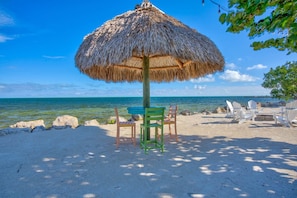 Une plage avec un parasol en chaume, une table avec des chaises et une vue sur la mer.