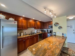 A kitchen with wooden cabinets, a granite countertop, stainless steel appliances, and a ceiling light fixture.