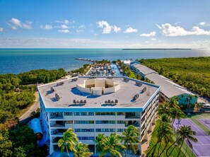 A multi-story hotel with a rooftop pool, surrounded by lush greenery and a view of the ocean.
