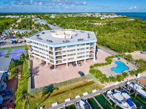 A multi-story hotel with a rooftop pool, surrounded by lush greenery and a clear view of the ocean.