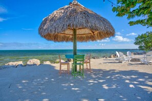 A beach with a thatched umbrella, a table with chairs, and a view of the sea. - Ocean/Marina View - Pool - Free Kayaks Pickleball (Key Largo)