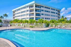 A hotel with a swimming pool, multiple balconies, and palm trees.