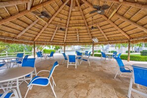 An outdoor patio with thatched roof, blue chairs, and tables.