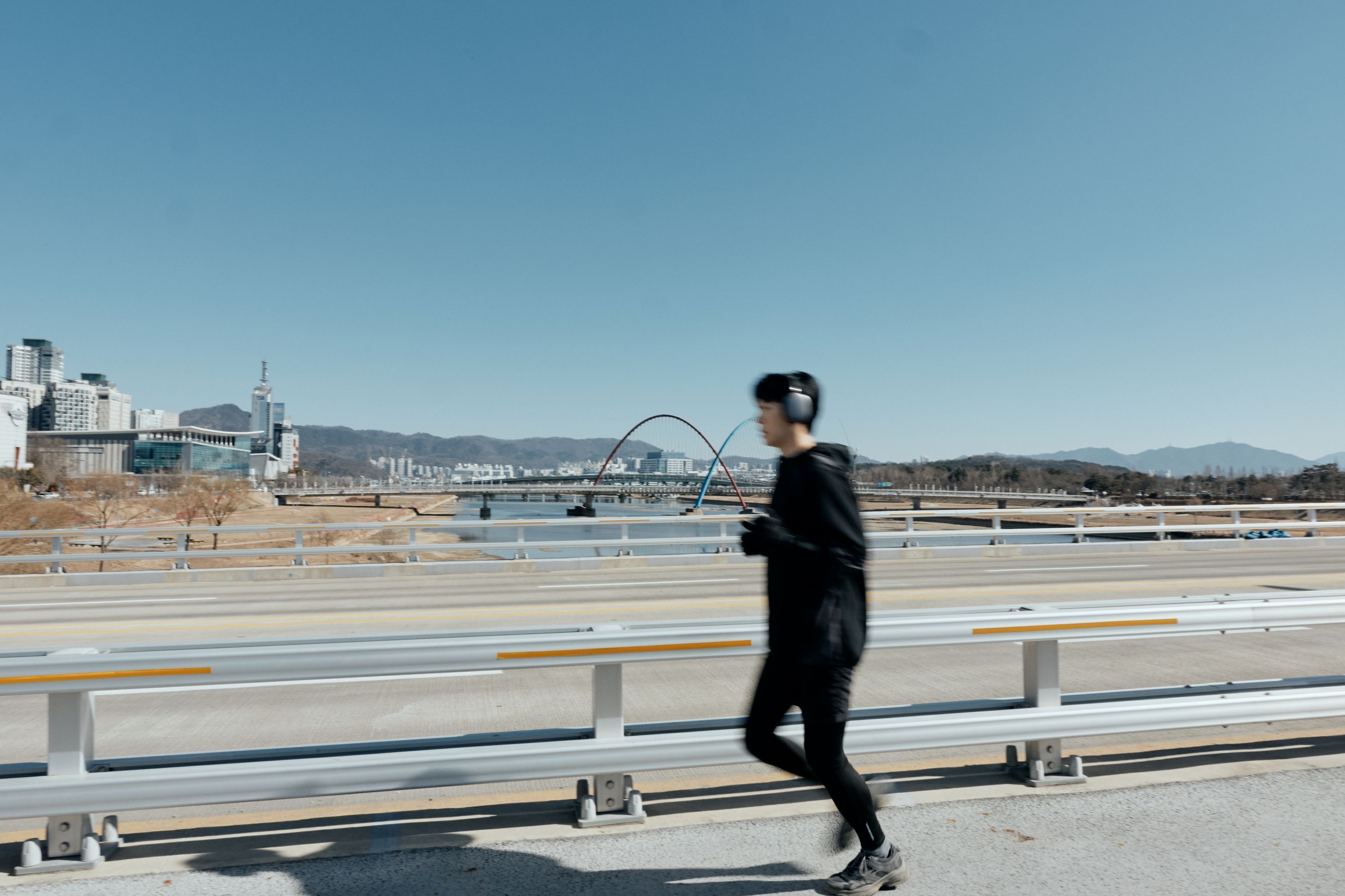 A person running on a bridge with a cityscape in the background.
